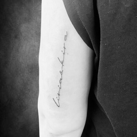 Feines Schriftzug-Tattoo entlang der Innenseite eines Oberarms.